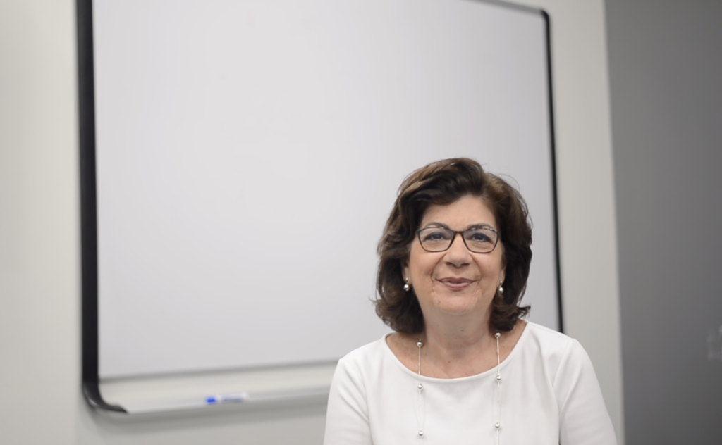 Photo of a professor sitting in front of white board in empty classroom