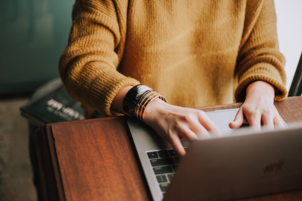 Person in yellow sweater sits typing at a laptop